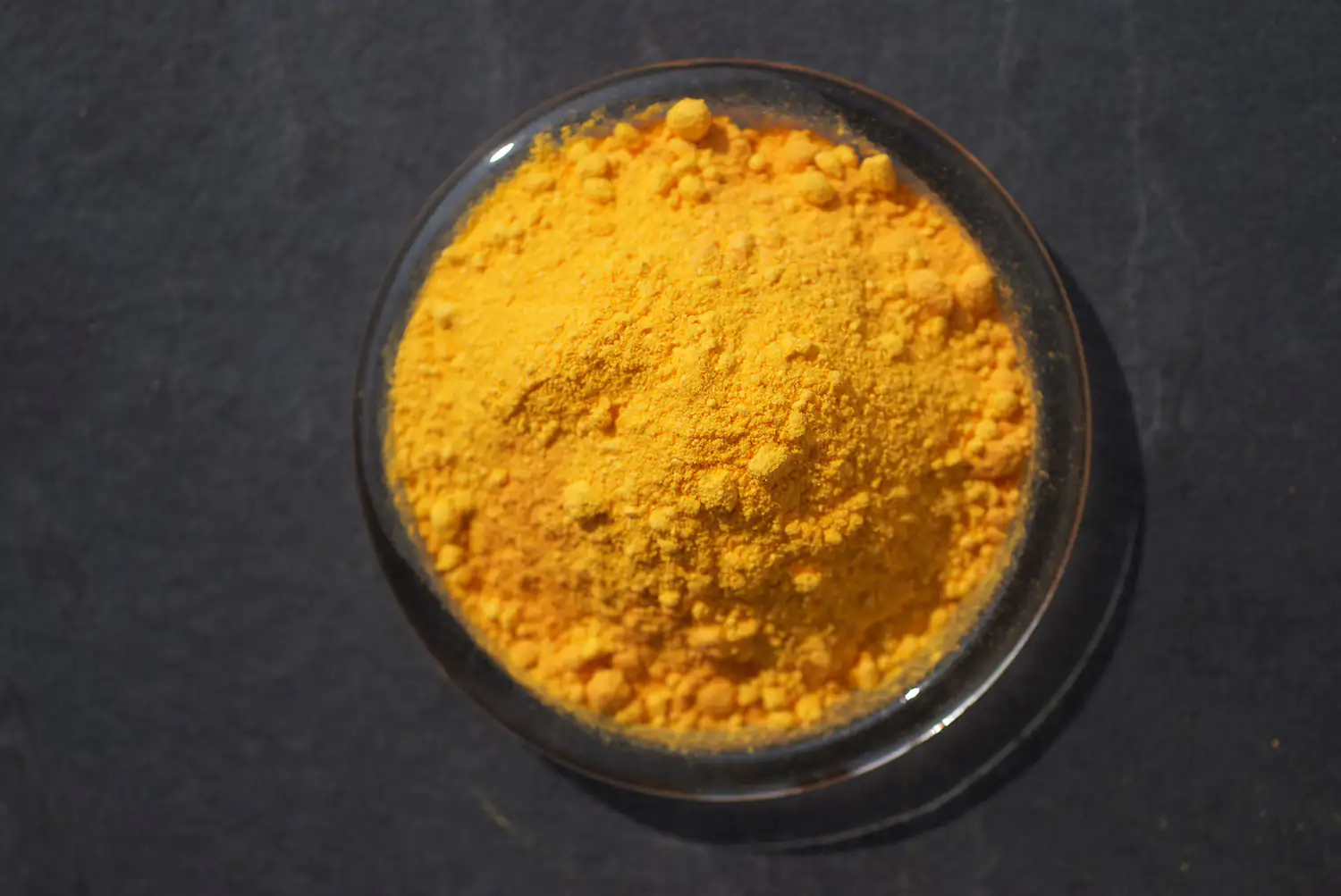 Finos y brillantes polvos de cúrcuma amarillos en un tazón transparente visto desde arriba.