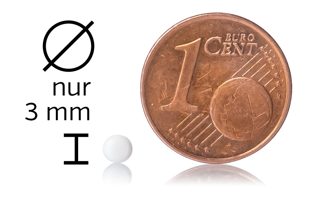Mikropíldora blanca de 3 mm de diámetro junto a una moneda de 1 céntimo sobre un fondo blanco.