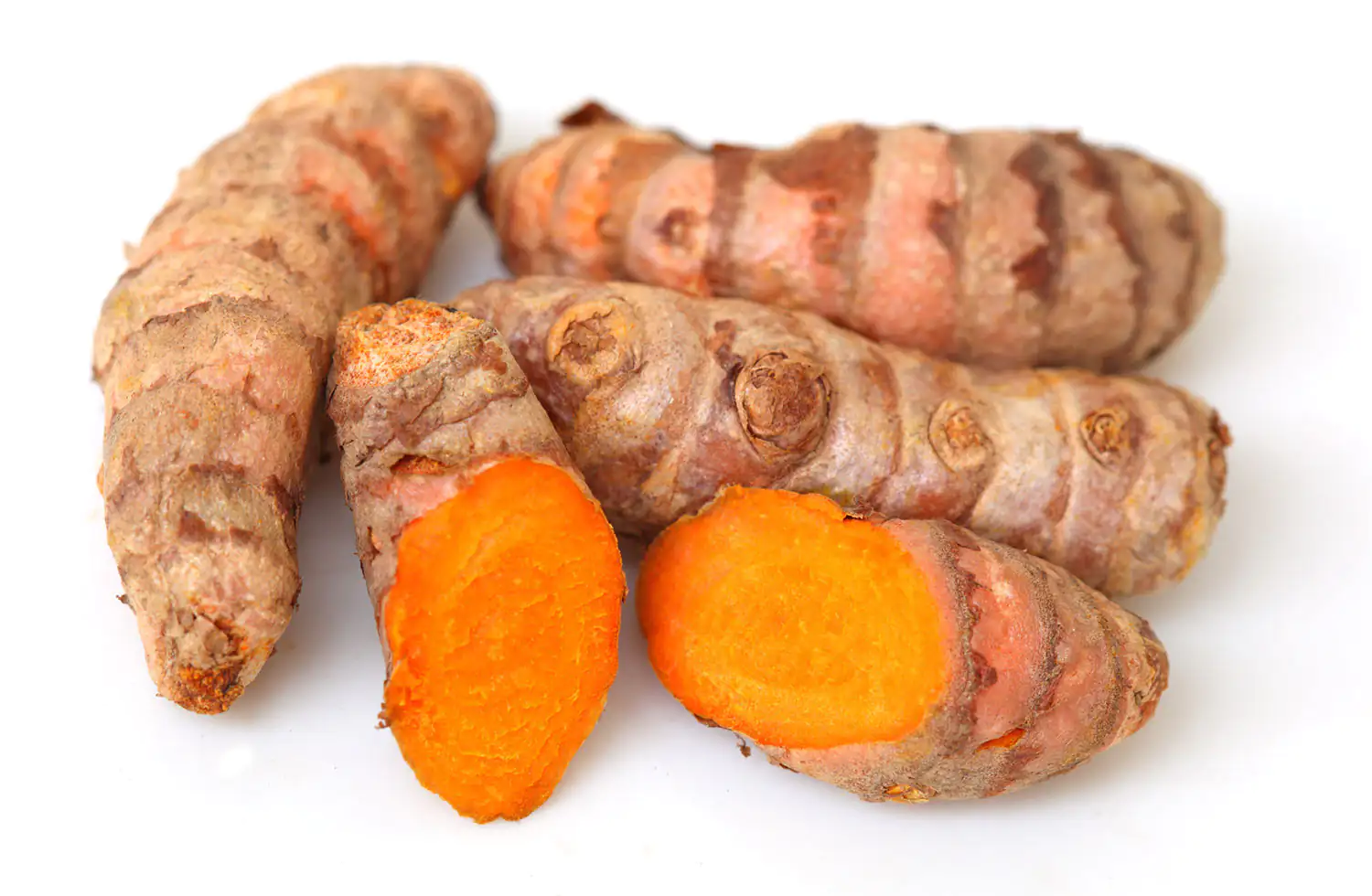 Raíces de Curcuma longa frescas Raíces frescas de cúrcuma sobre fondo blanco, algunas cortadas por la mitad, mostrando pulpa naranja, un total de cinco piezas.