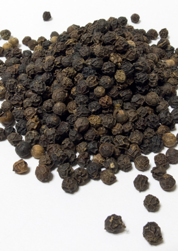 Un montón de granos de pimienta negra sobre un fondo blanco, esparcidos, de diferentes tamaños y colores.