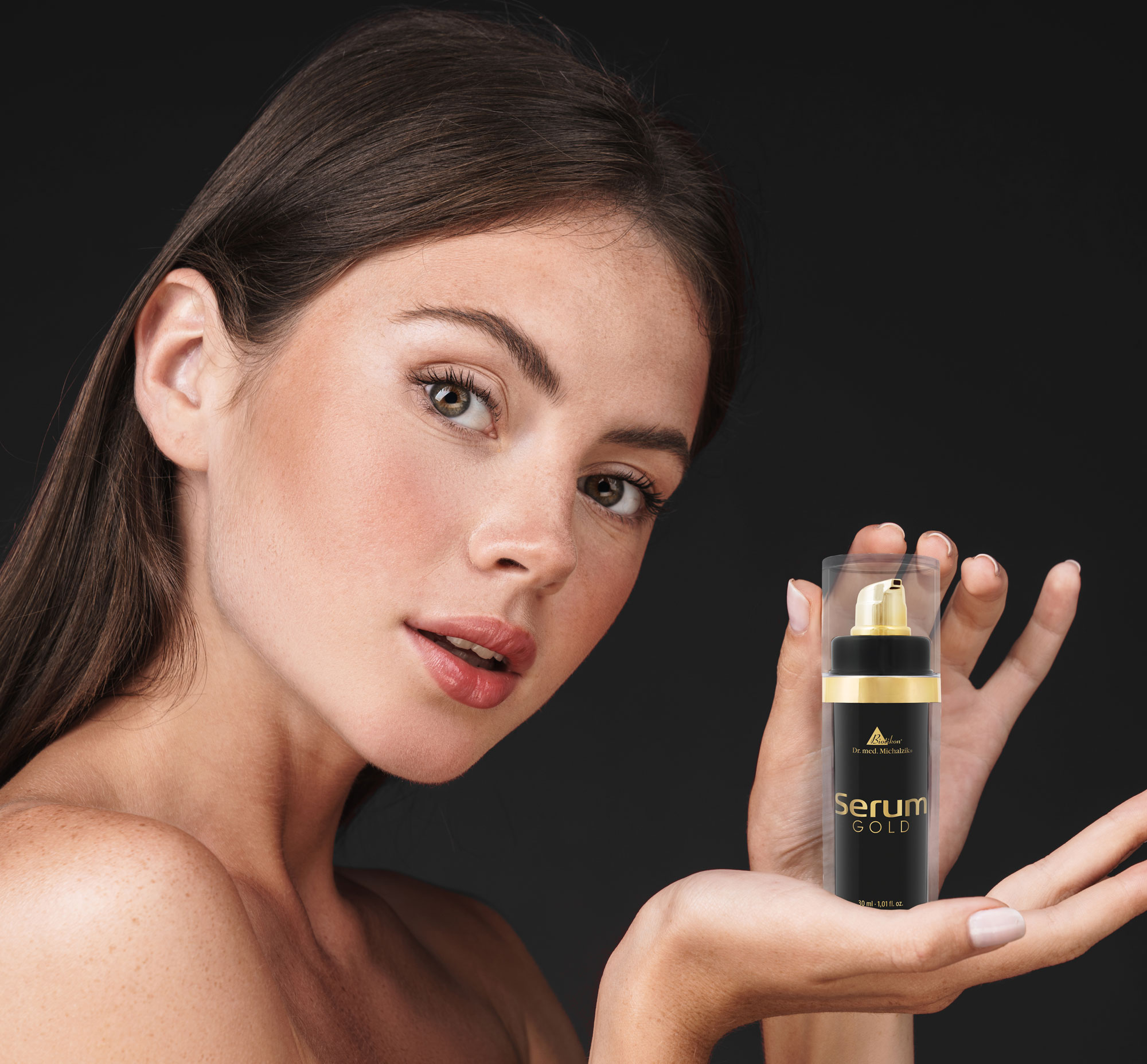 Suero facial en una elegante botella con bomba de 30 ml, empaquetado en negro y dorado, presentado en la mano de una mujer.