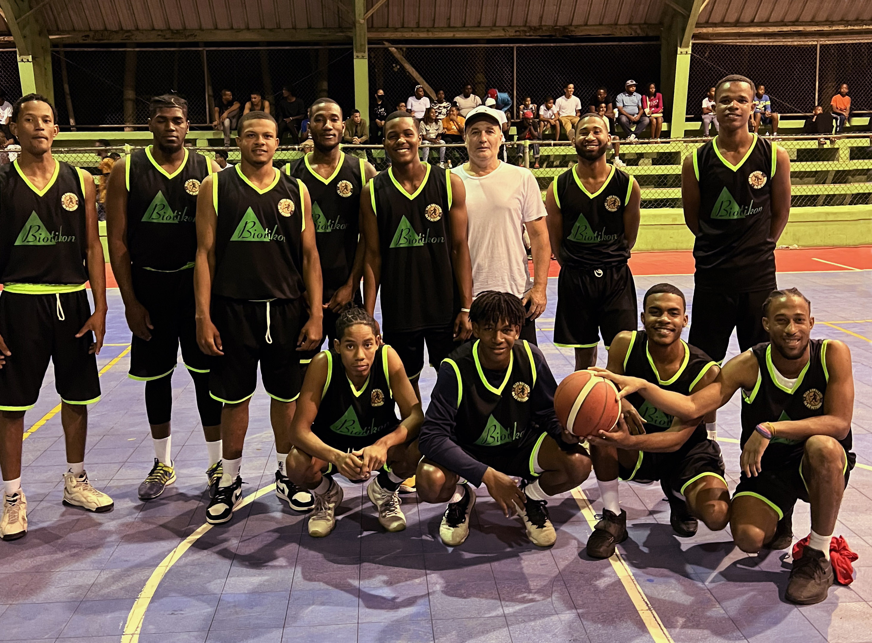 Equipo de baloncesto – Foto de grupo Un grupo de jugadores de baloncesto en camisetas negras con acentos verdes, de pie en la cancha con un balón de baloncesto y una pose de celebración.