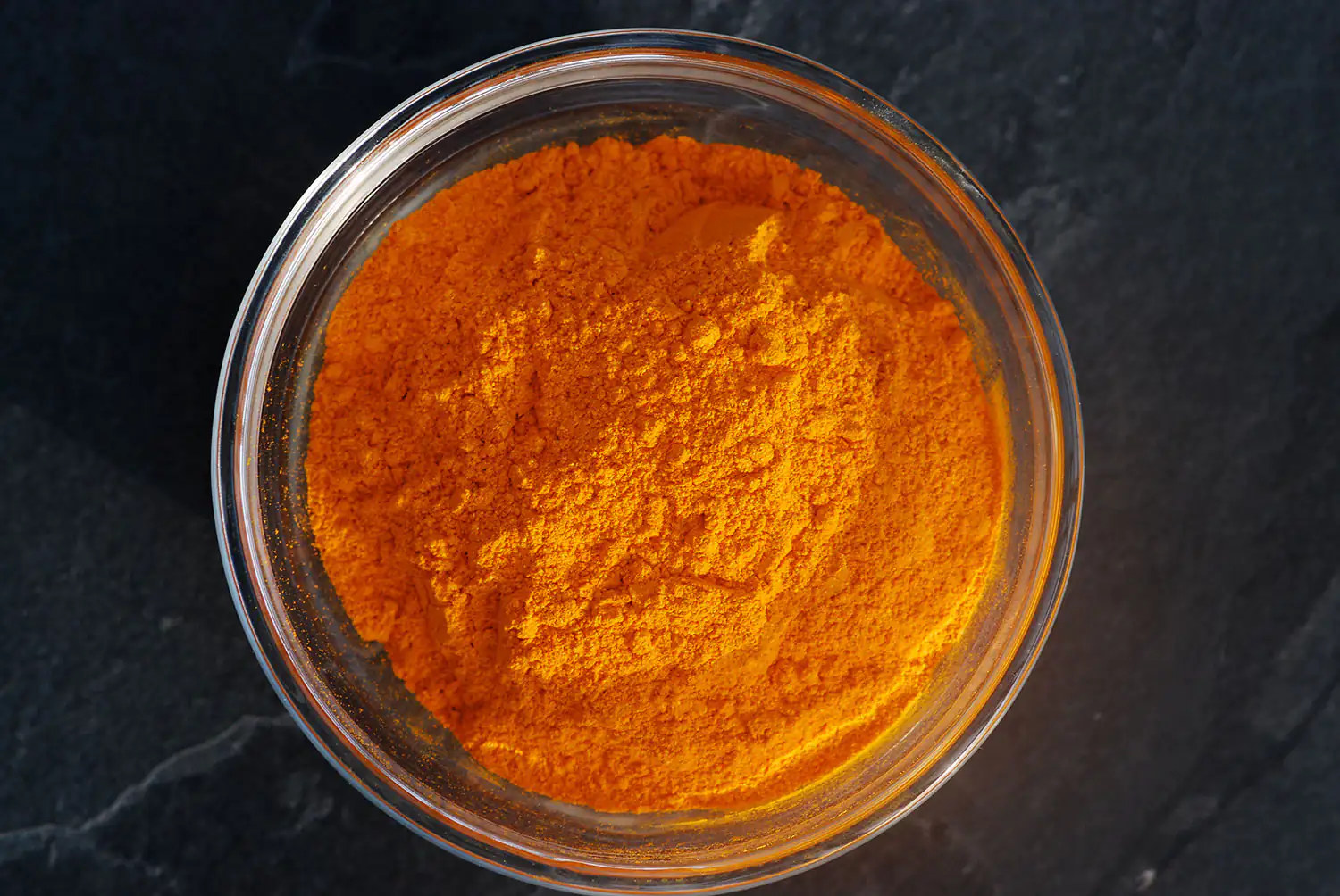 Polvo de cúrcuma naranja en un frasco de vidrio, 100 g, tomado desde arriba.