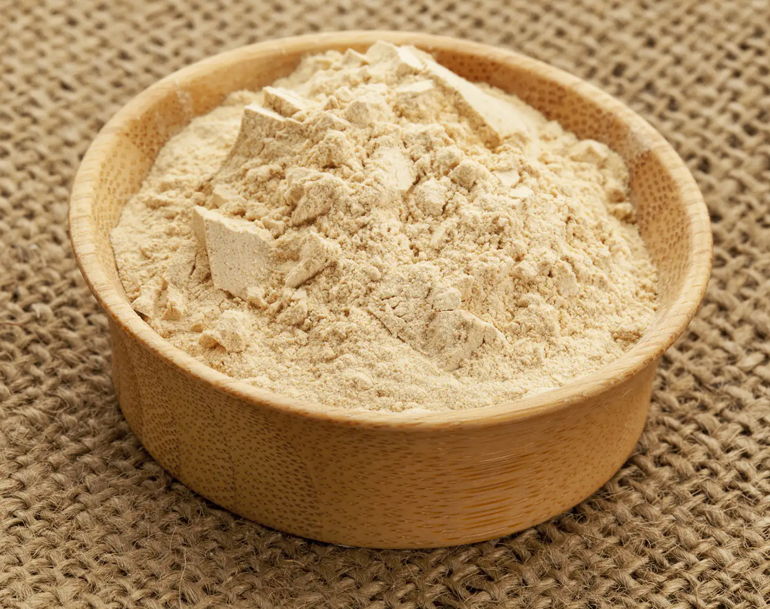 Maca en Polvo - Superalimento Energético Maca en polvo finamente molido en un bol de madera, color beige, sobre una superficie de yute.